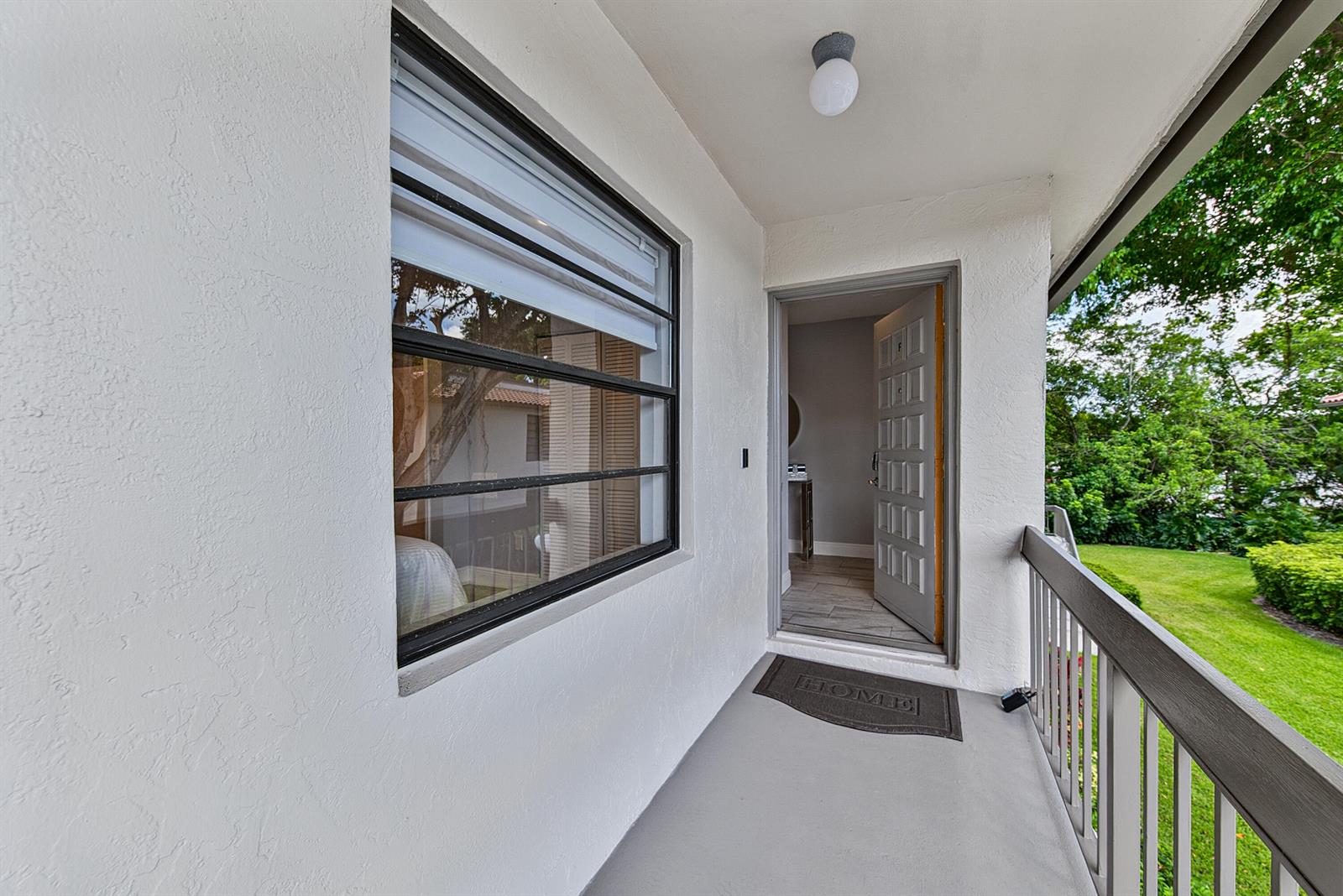 A balcony with a window, an open door, and a railing overlooking a grassy yard — 21656 Juego Circle S # 23f, Boca Raton FL 33433, BOCA RATON, FL