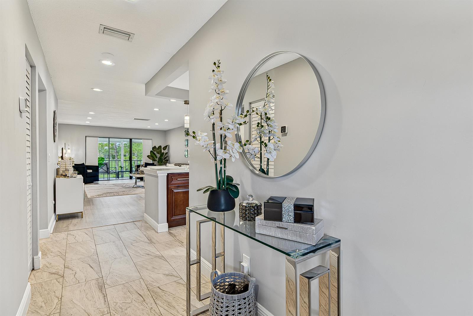 A hallway features a glass console table, a round mirror, and tile flooring — 21656 Juego Circle S # 23f, Boca Raton FL 33433, BOCA RATON, FL