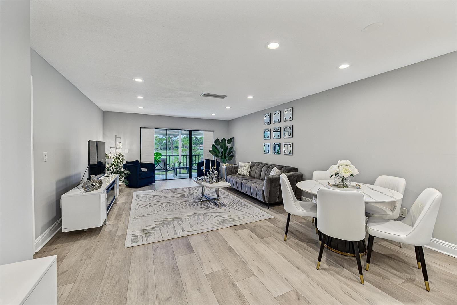 A modern living and dining room with gray walls, wood floors, and a sliding glass door — 21656 Juego Circle S # 23f, Boca Raton FL 33433, BOCA RATON, FL