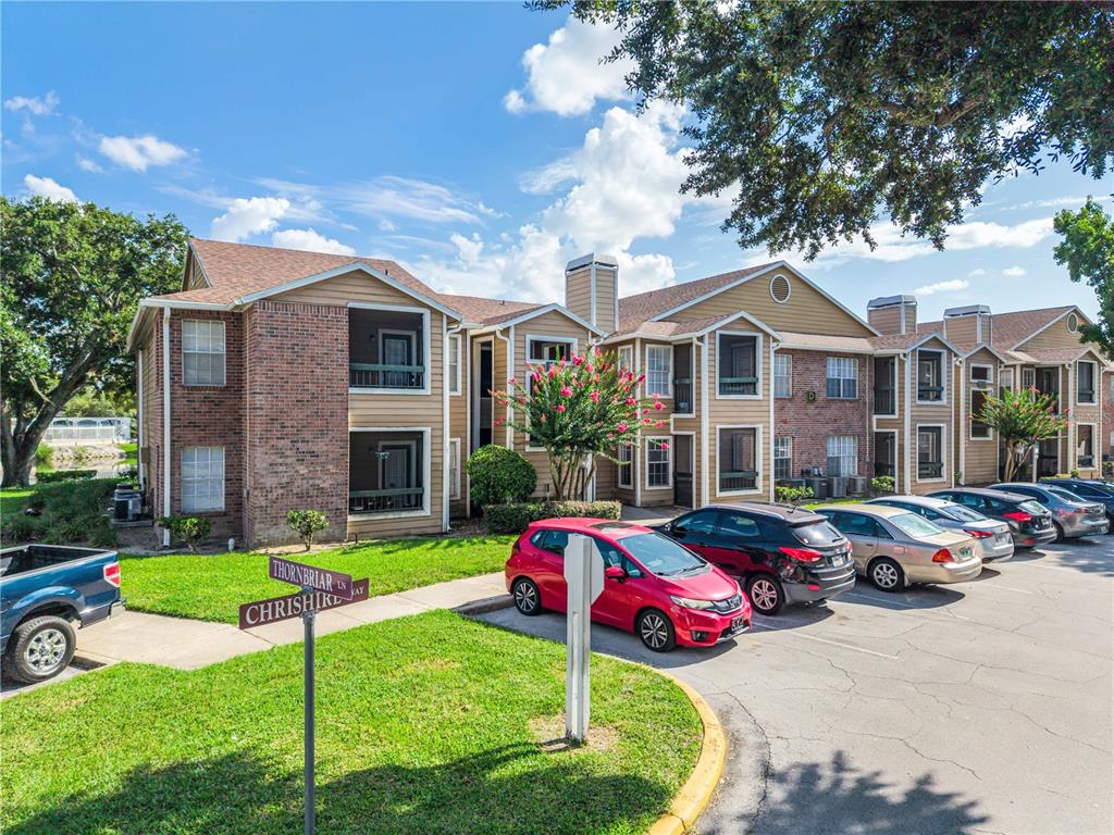 A multi-story apartment building with brick and tan siding sits behind a parking lot — 5530 CHRISHIRE WAY UNIT D109, ORLANDO, FL