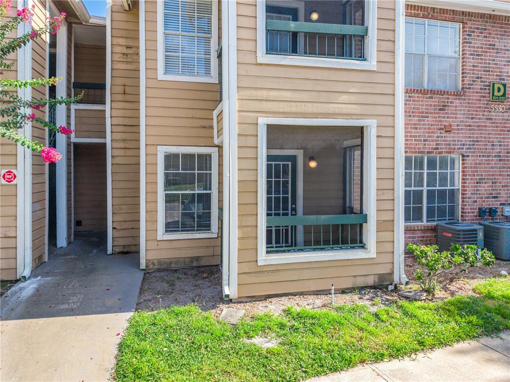 A two-story apartment building exterior features tan siding, a screened-in porch, and brick accents — 5530 CHRISHIRE WAY UNIT D109, ORLANDO, FL