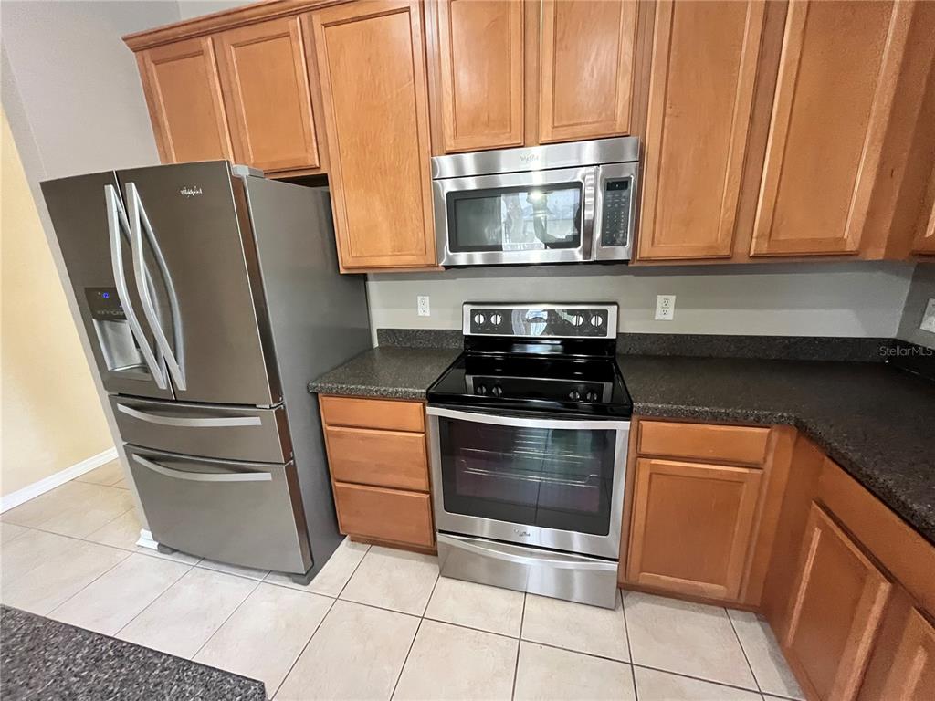 A kitchen features wood cabinets, stainless steel appliances, and dark countertops over tiled flooring — 919 MAGNOLIA BLOSSOM COURT, APOPKA, FL