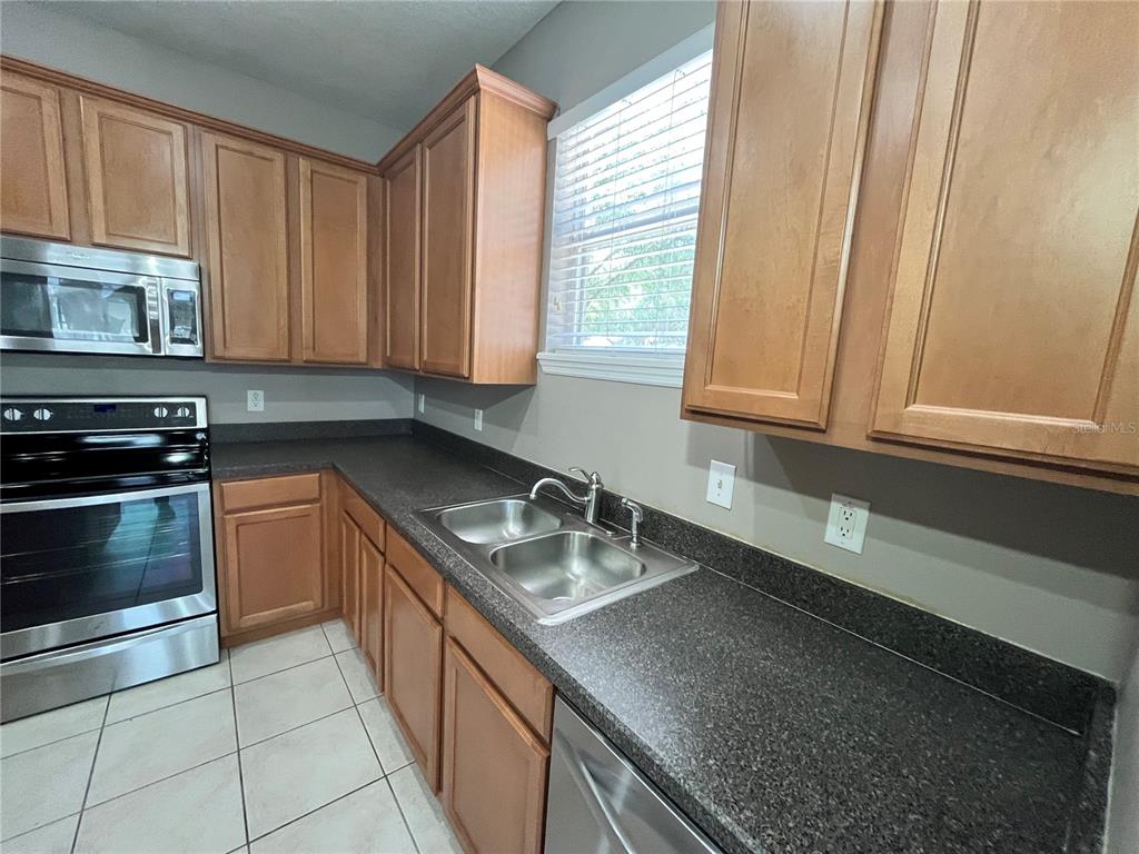 A kitchen features wood cabinets, stainless steel appliances, a center island, and tile flooring — 919 MAGNOLIA BLOSSOM COURT, APOPKA, FL