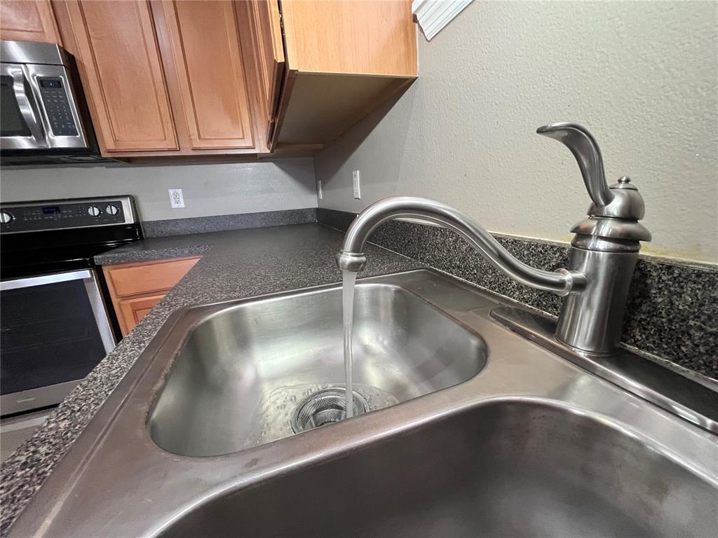 A stainless steel kitchen sink with a running faucet sits in a dark laminate countertop — 919 MAGNOLIA BLOSSOM COURT, APOPKA, FL