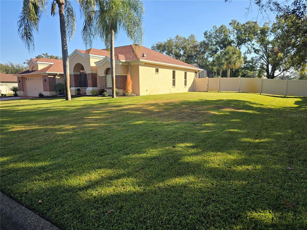 A single-story house with a tan stucco exterior, brick accents, and a large front lawn — 1030 ROWLAND PICKERT LANE, LUTZ, FL