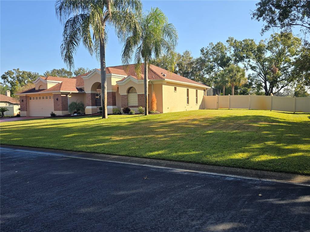 A single-story house with a tan stucco exterior, brick accents, and palm trees in front — 1030 ROWLAND PICKERT LANE, LUTZ, FL