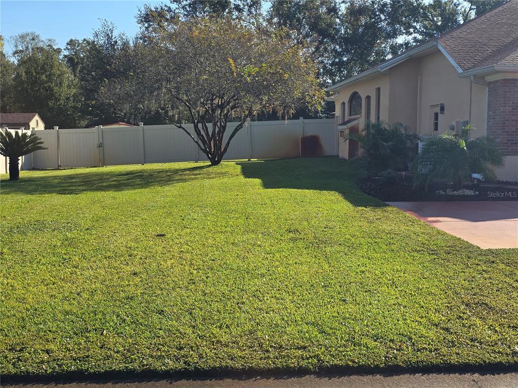A grassy side yard features a large tree, a white vinyl fence, and landscaping — 1030 ROWLAND PICKERT LANE, LUTZ, FL