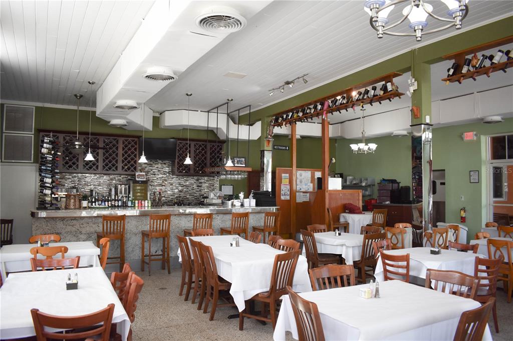 A restaurant dining room features white-clothed tables, wooden chairs, a bar area, and green walls — 1618 E 5TH AVENUE, TAMPA, FL