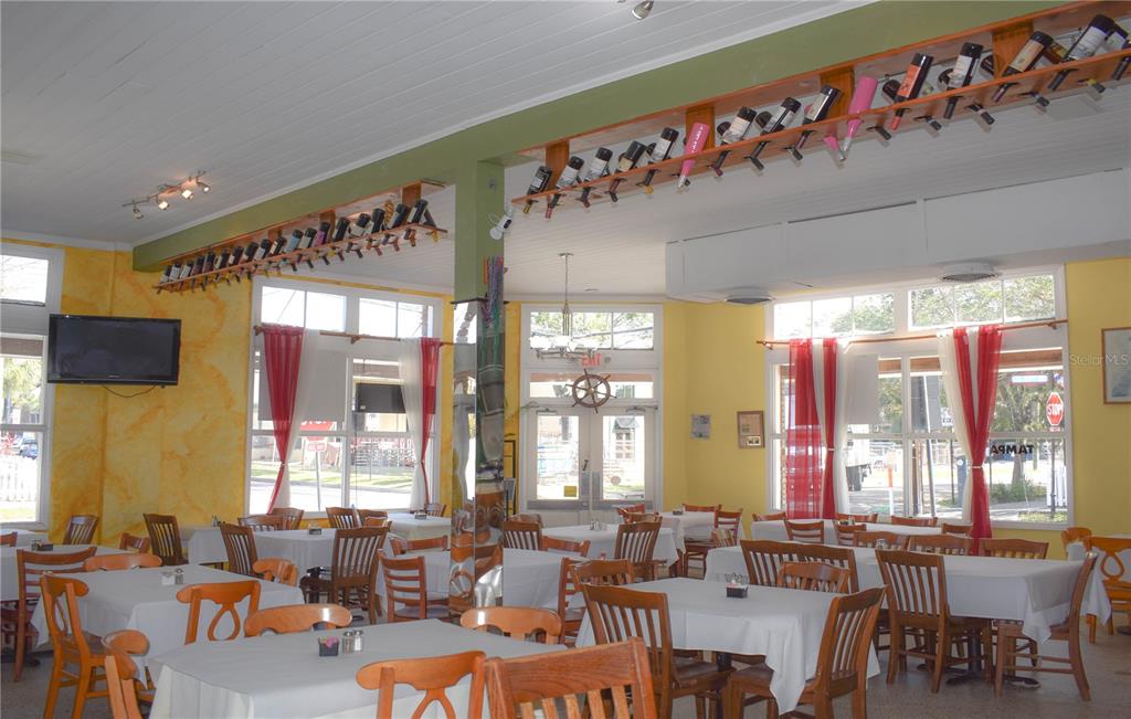 A restaurant dining room features yellow walls, white tablecloths, and wine bottles displayed on overhead racks — 1618 E 5TH AVENUE, TAMPA, FL