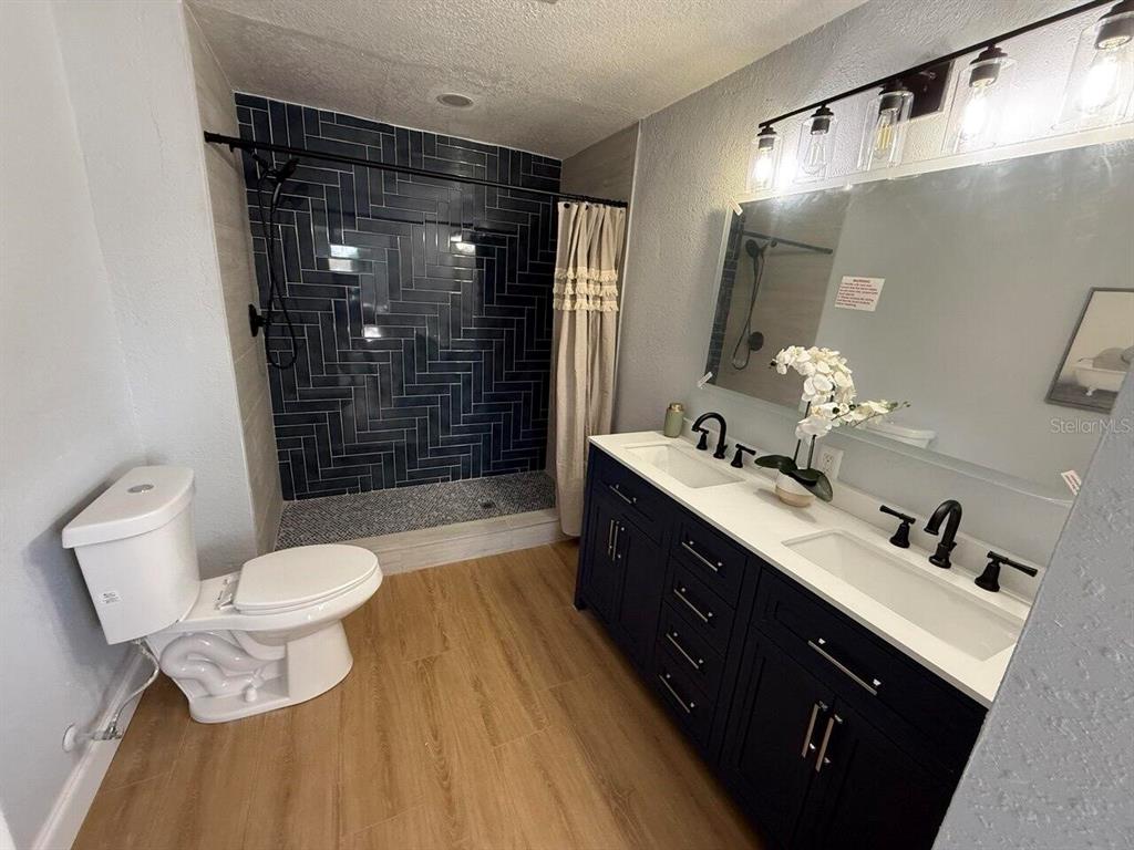 A bathroom features a dark blue herringbone-tiled shower, a double vanity, and wood-look flooring — 369 WESTWINDS DRIVE, PALM HARBOR, FL