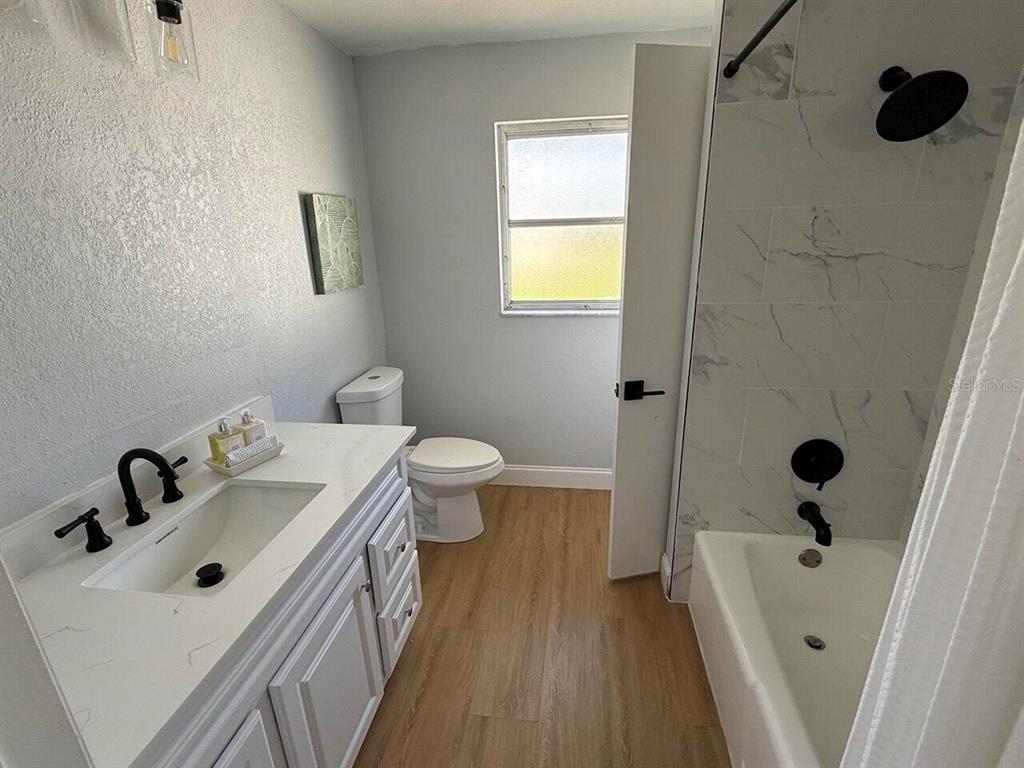 A bathroom features a white vanity, a toilet, and a tub with marble-look tile walls — 369 WESTWINDS DRIVE, PALM HARBOR, FL