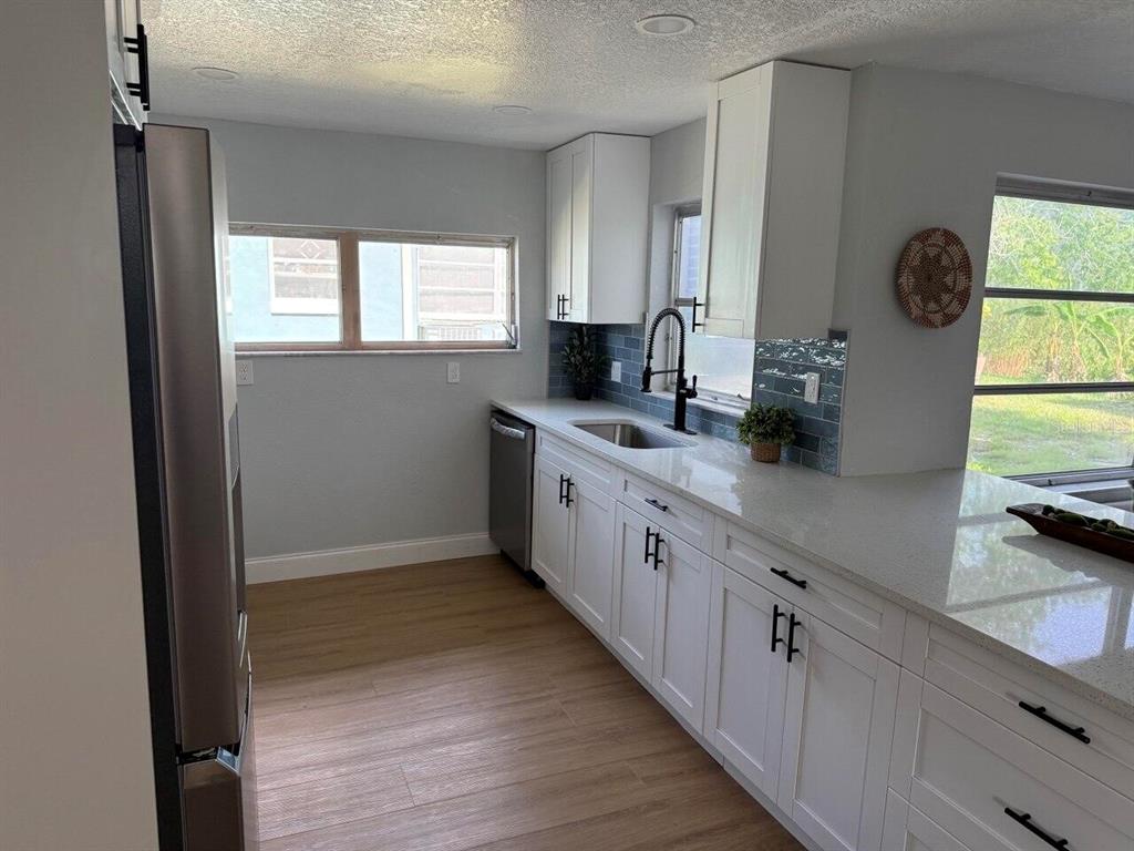 A kitchen features white cabinetry, quartz countertops, a blue tiled backsplash, and stainless steel appliances — 369 WESTWINDS DRIVE, PALM HARBOR, FL
