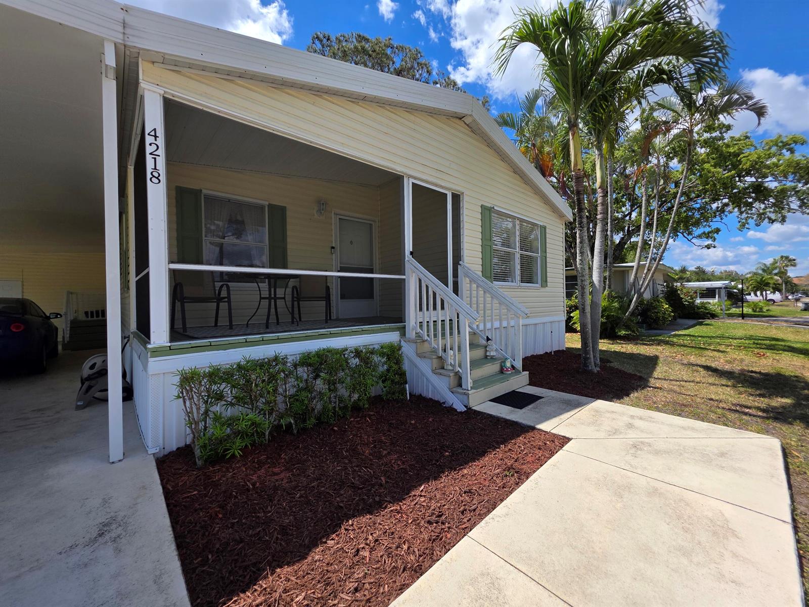 A light yellow manufactured home features a screened-in front porch, a carport, and palm trees — 4218 6th Court, Lantana FL 33462, LANTANA, FL