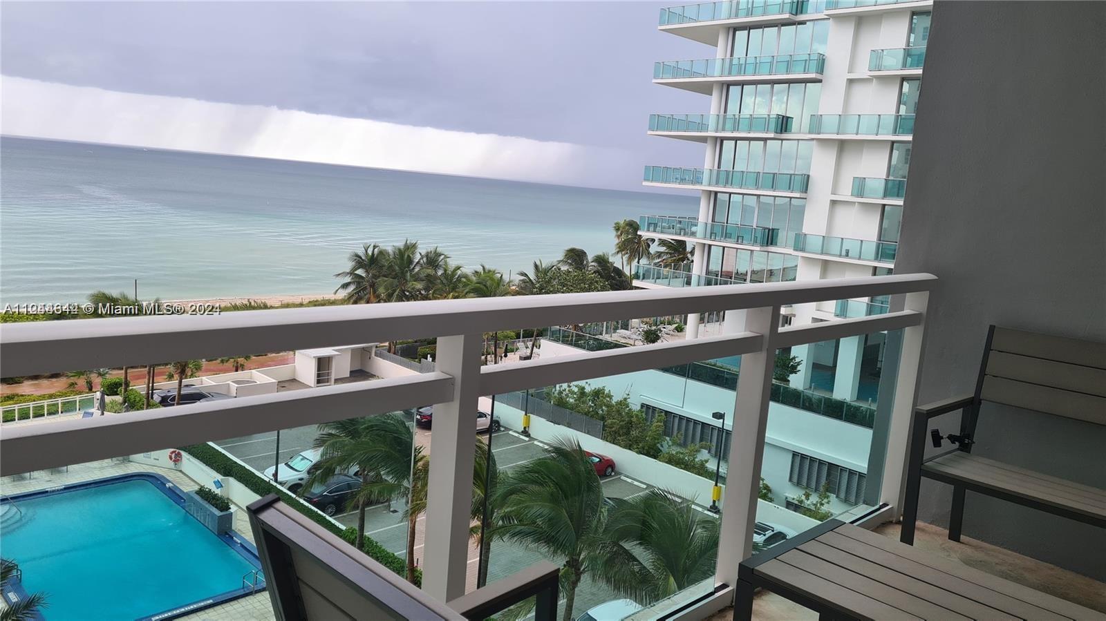 A balcony view overlooks a swimming pool, parking lot, and the ocean under a cloudy sky — 6917 Collins Ave # 809, Miami Beach FL 33141, MIAMI BEACH, FL