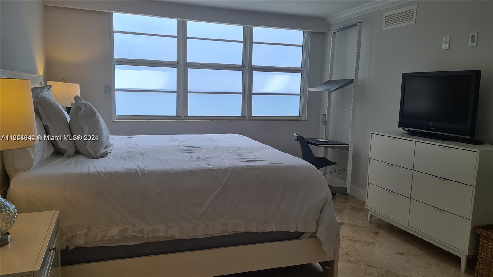 A bedroom features a bed, a white dresser with a television, and a window view — 6917 Collins Ave # 809, Miami Beach FL 33141, MIAMI BEACH, FL