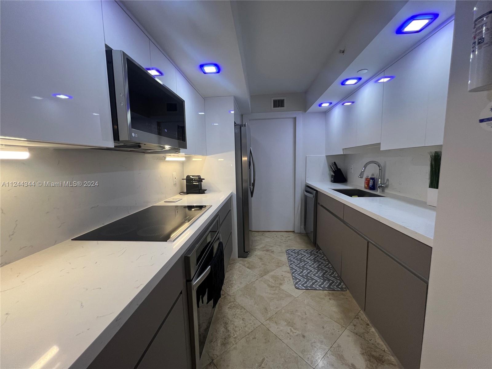 A galley kitchen features white upper cabinets, grey lower cabinets, marble-look countertops, and blue recessed lighting — 6917 Collins Ave # 809, Miami Beach FL 33141, MIAMI BEACH, FL