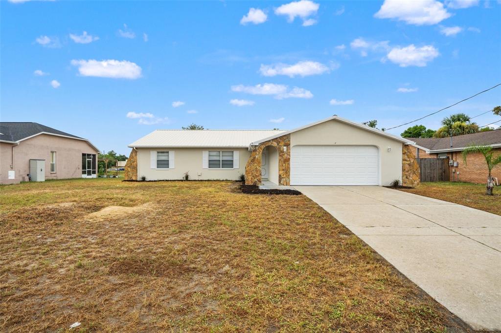 A single-story house with a white garage, stone accents, and a dry, grassy front yard — 5510 ALDERWOOD STREET, SPRING HILL, FL