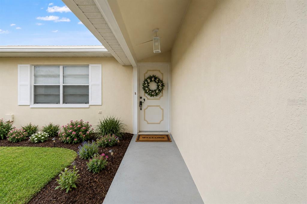 A white front door with a wreath and welcome mat sits under a covered entryway — 5510 ALDERWOOD STREET, SPRING HILL, FL