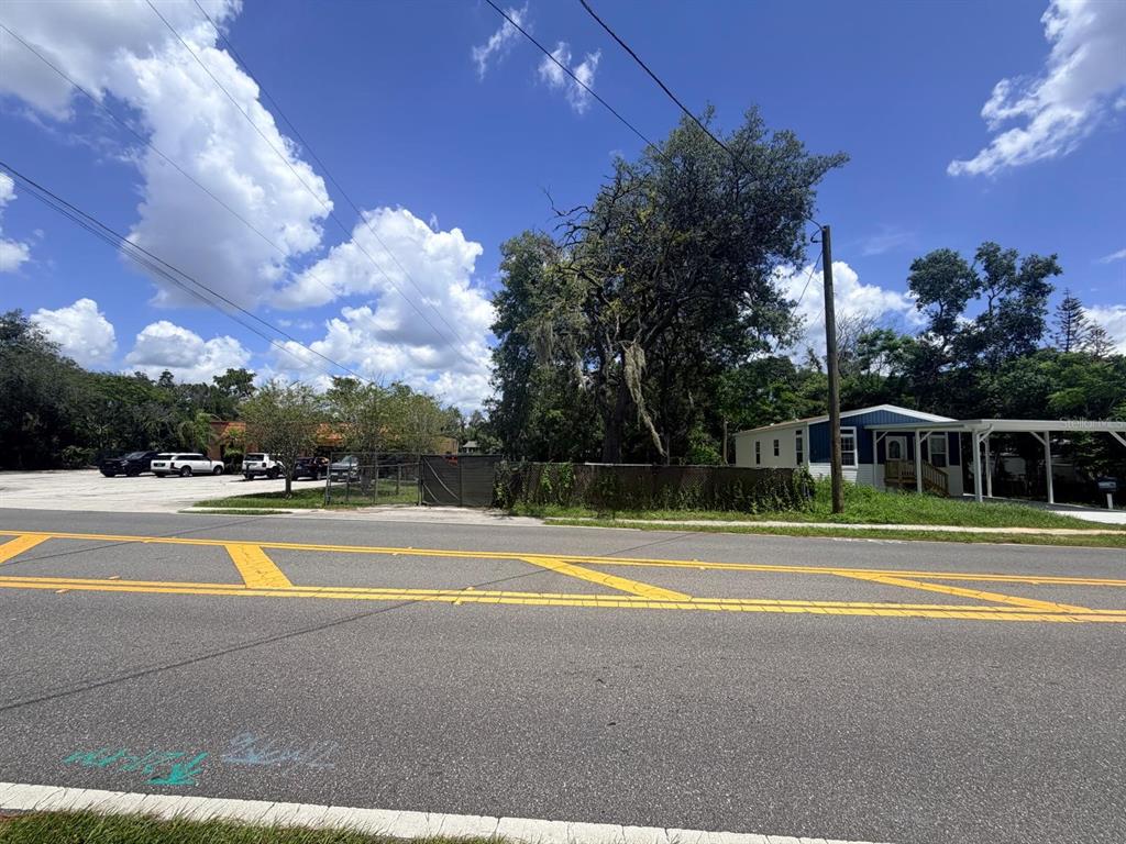 A paved road runs in front of a fenced lot with trees and a mobile home — 1329 LAKE DRIVE, CASSELBERRY, FL