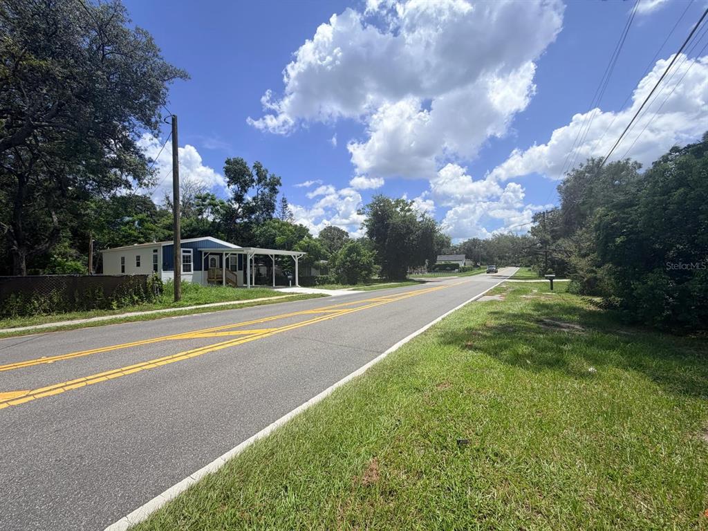 A single-story manufactured home with a carport sits beside a paved road under a cloudy sky — 1329 LAKE DRIVE, CASSELBERRY, FL