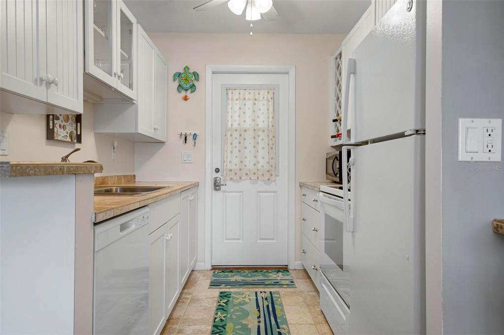 A galley kitchen features white cabinets, light countertops, a white refrigerator, and a back door — 3808 GULF OF MEXICO DRIVE UNIT E205, LONGBOAT KEY, FL