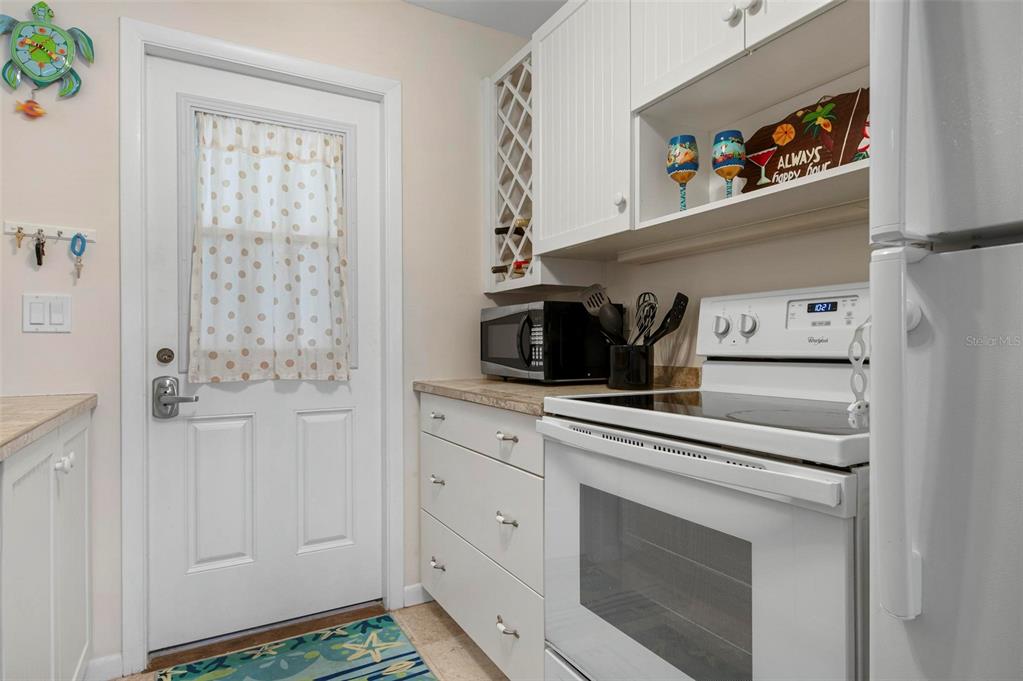 A white kitchen features a stove, microwave, cabinetry, and a door with a patterned curtain — 3808 GULF OF MEXICO DRIVE UNIT E205, LONGBOAT KEY, FL