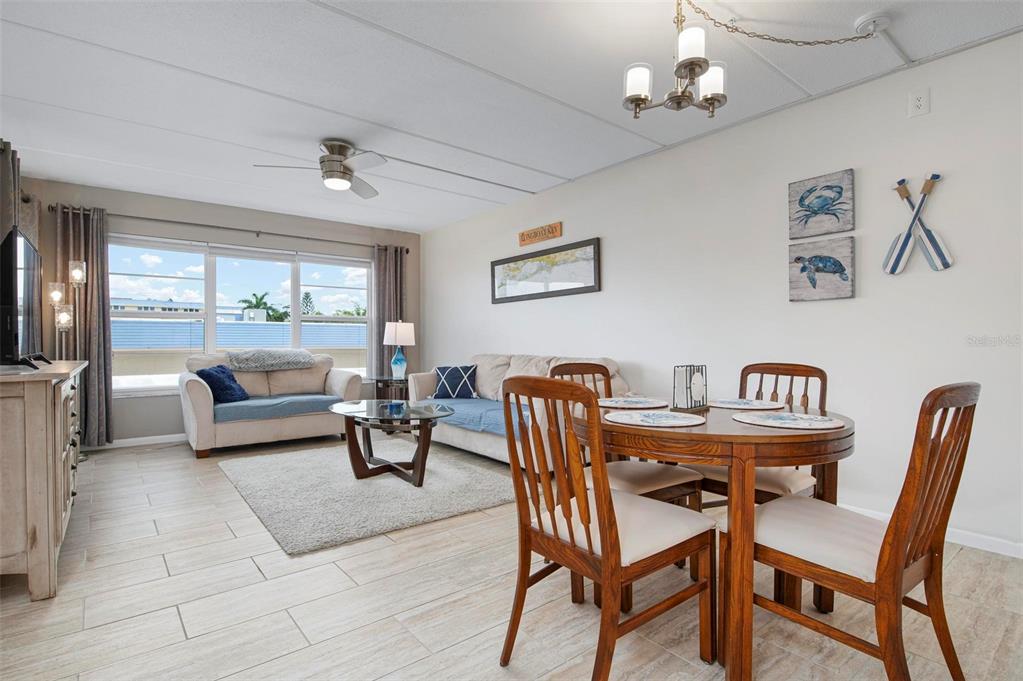 This living and dining area features tile flooring, a ceiling fan, and coastal wall decor — 3808 GULF OF MEXICO DRIVE UNIT E205, LONGBOAT KEY, FL