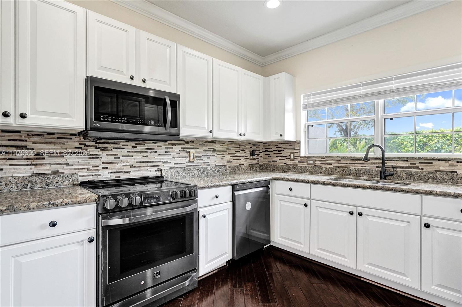 A kitchen features white cabinets, stainless steel appliances, granite countertops, and a tile backsplash — 4501 Windmill Palm Way, Green Acres FL 33463, GREEN ACRES, FL