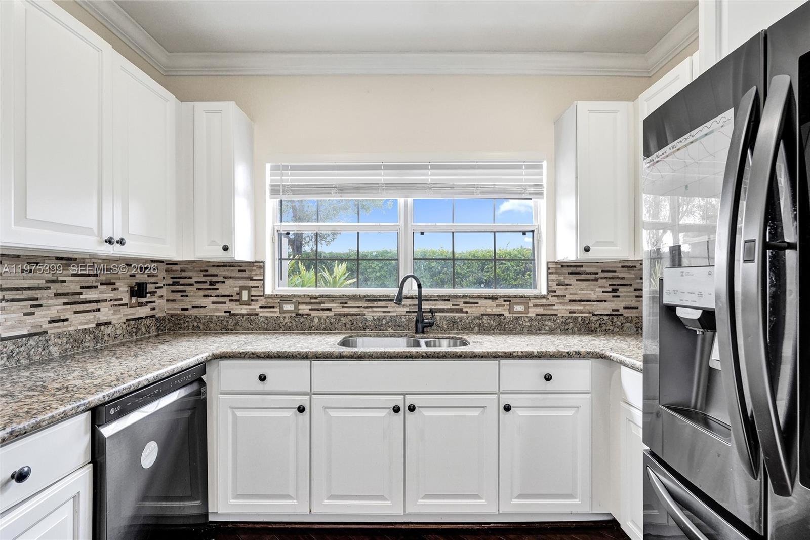 A kitchen features white cabinets, granite countertops, a tiled backsplash, and a stainless steel refrigerator — 4501 Windmill Palm Way, Green Acres FL 33463, GREEN ACRES, FL