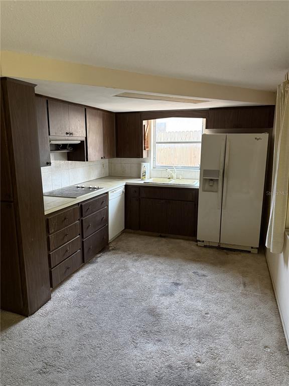 A kitchen with dark wood cabinets, white appliances, and carpeted flooring — 9401 GRAY FOX LANE, PORT RICHEY, FL