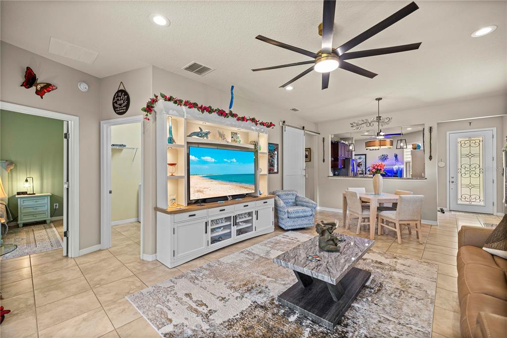 A living room features a large entertainment center, a ceiling fan, and tile flooring — 7684 SW 94TH CIRCLE, OCALA, FL