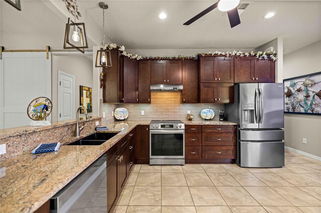A kitchen features dark wood cabinets, granite countertops, stainless steel appliances, and tile flooring — 7684 SW 94TH CIRCLE, OCALA, FL