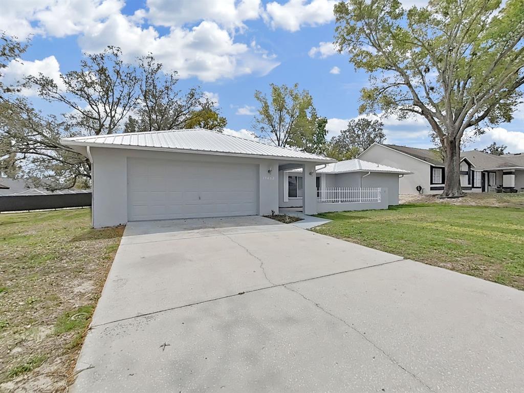 A single-story house with a white metal roof, gray exterior, and a concrete driveway — 10452 FORDHAM STREET, SPRING HILL, FL