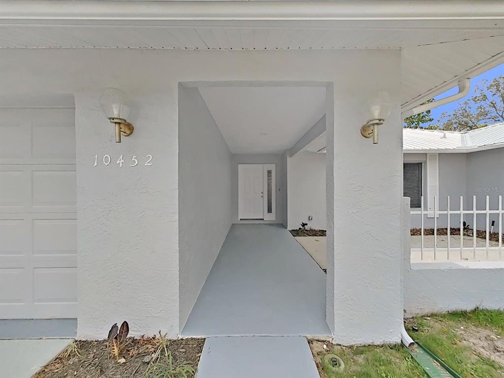 A white house exterior features a covered entryway with a gray floor and address numbers — 10452 FORDHAM STREET, SPRING HILL, FL