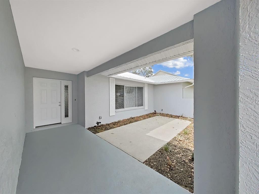 A covered entryway features a gray concrete floor, a white front door, and a patio — 10452 FORDHAM STREET, SPRING HILL, FL
