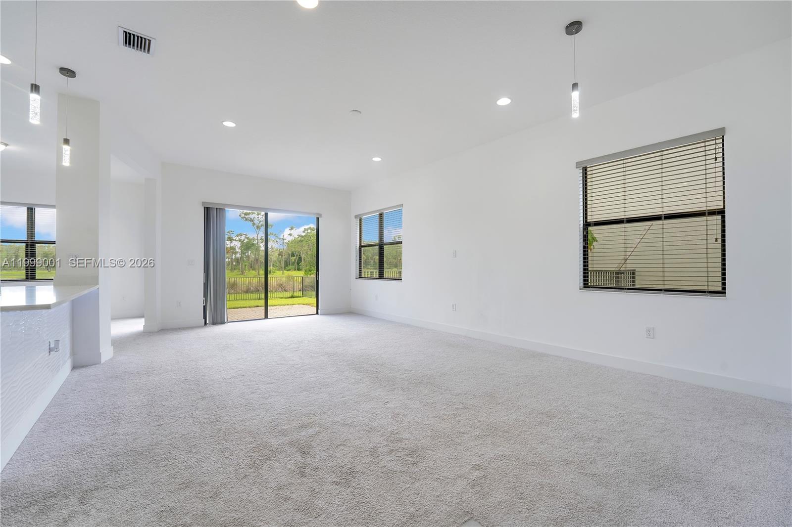 A bright, carpeted living area features white walls, recessed lighting, pendant lights, and sliding doors — 5546 Agostino Way, Ave Maria FL 34142, AVE MARIA, FL