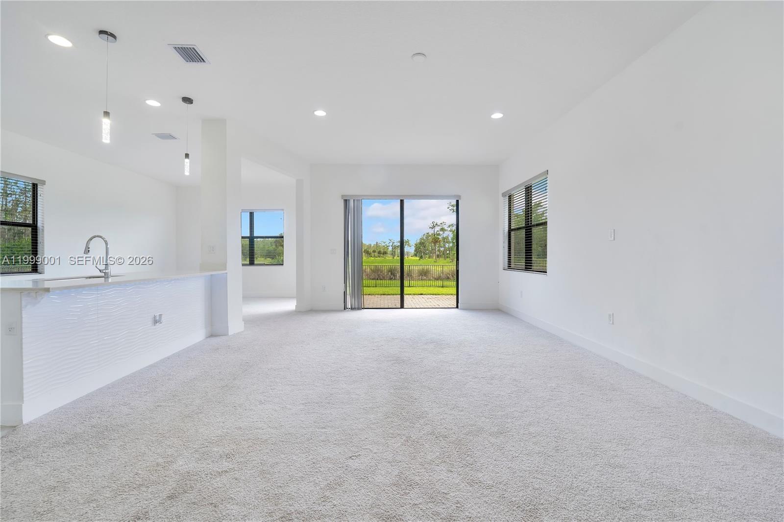 A bright, carpeted living area features a kitchen island, sliding glass doors, and large windows — 5546 Agostino Way, Ave Maria FL 34142, AVE MARIA, FL