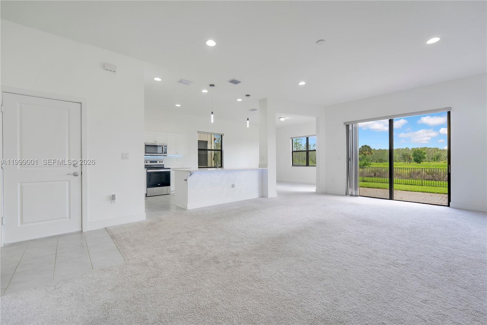 A bright, open-concept living area features white walls, carpeted flooring, and a kitchen with an island — 5546 Agostino Way, Ave Maria FL 34142, AVE MARIA, FL