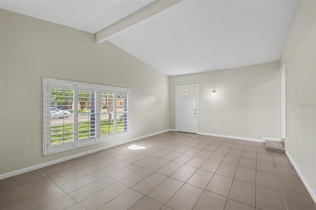 An empty room features light-colored walls, large windows with white shutters, and tiled flooring — 722 GALSWORTHY AVENUE, ORLANDO, FL