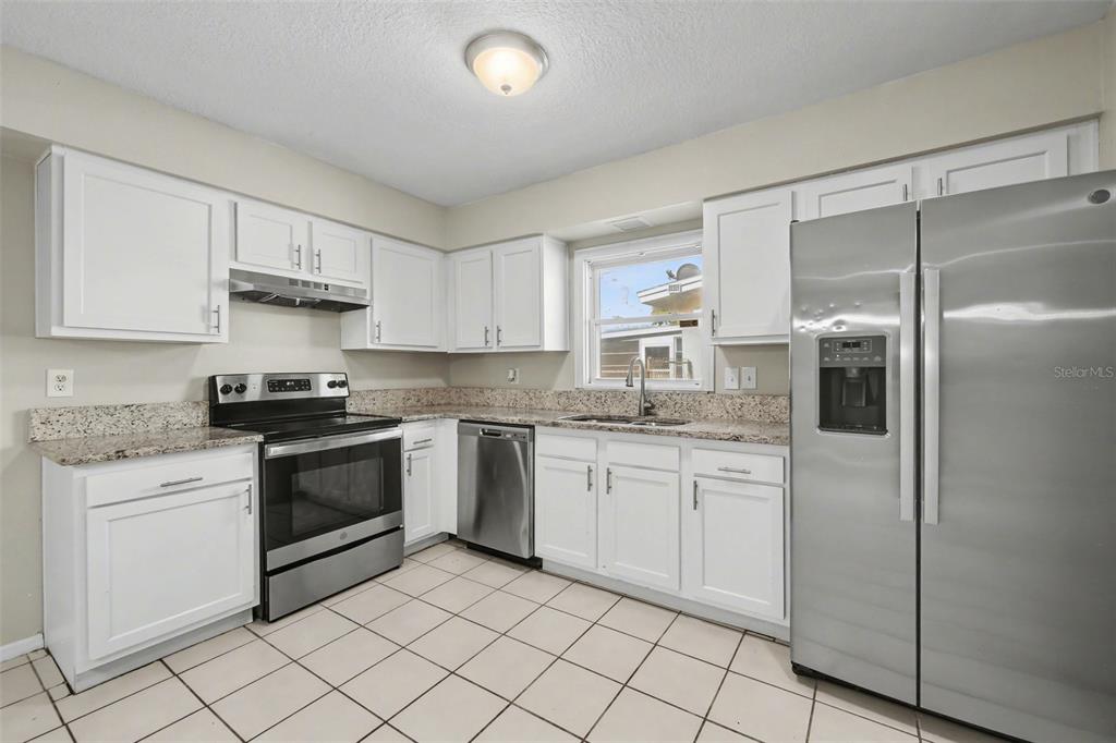 A kitchen with white cabinets, granite countertops, stainless steel appliances, and light-colored tile flooring — 722 GALSWORTHY AVENUE, ORLANDO, FL