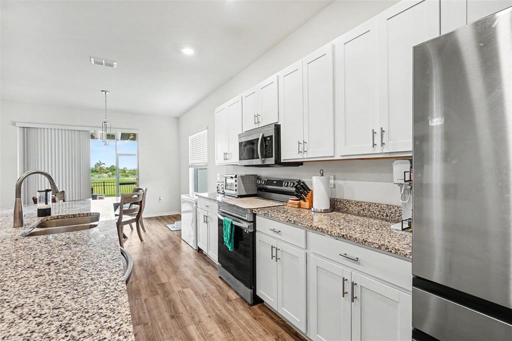 A kitchen with white cabinets, granite countertops, stainless steel appliances, and wood-look flooring — 6103 HAMMOCK ISLAND WAY, HAINES CITY, FL
