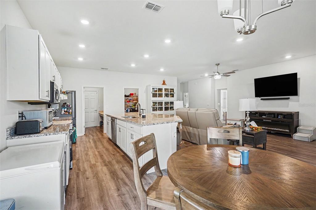 An open-concept kitchen and living area features white cabinetry, a granite island, and wood flooring — 6103 HAMMOCK ISLAND WAY, HAINES CITY, FL