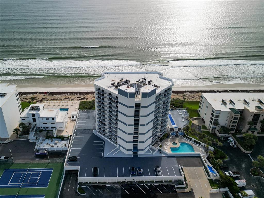 An aerial view shows a multi-story beachfront condominium building with a pool and parking lot — 5207 S ATLANTIC AVENUE UNIT 426, NEW SMYRNA BEACH, FL