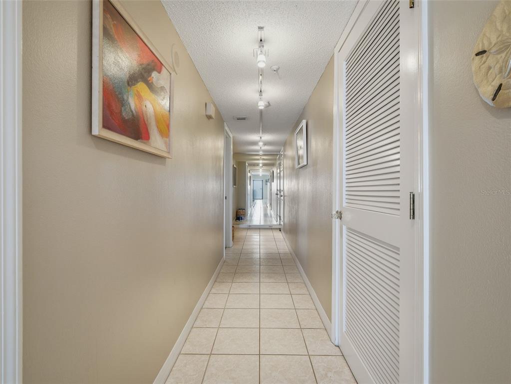 A long hallway features beige walls, tiled flooring, track lighting, and a white louvered door — 5207 S ATLANTIC AVENUE UNIT 426, NEW SMYRNA BEACH, FL