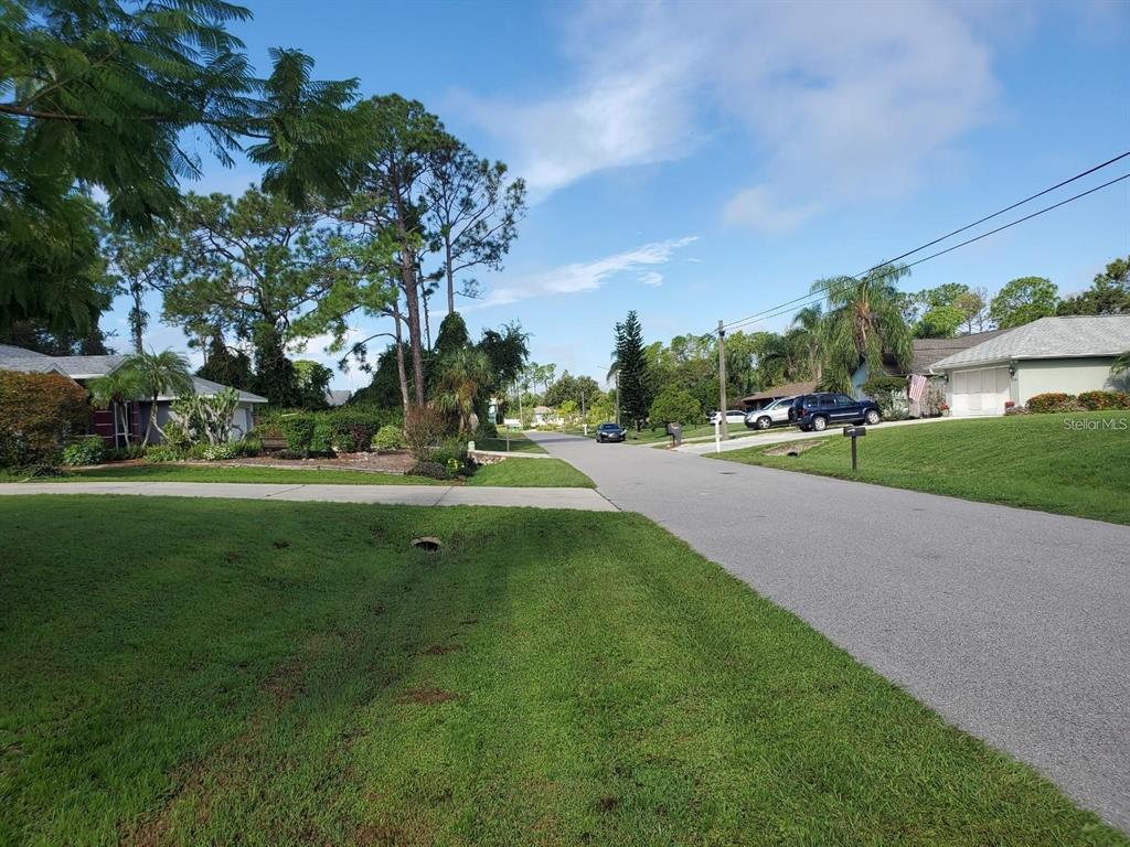 A residential street view featuring houses, green lawns, trees, and parked cars under a blue sky — SLAYTON AVENUE, NORTH PORT, FL