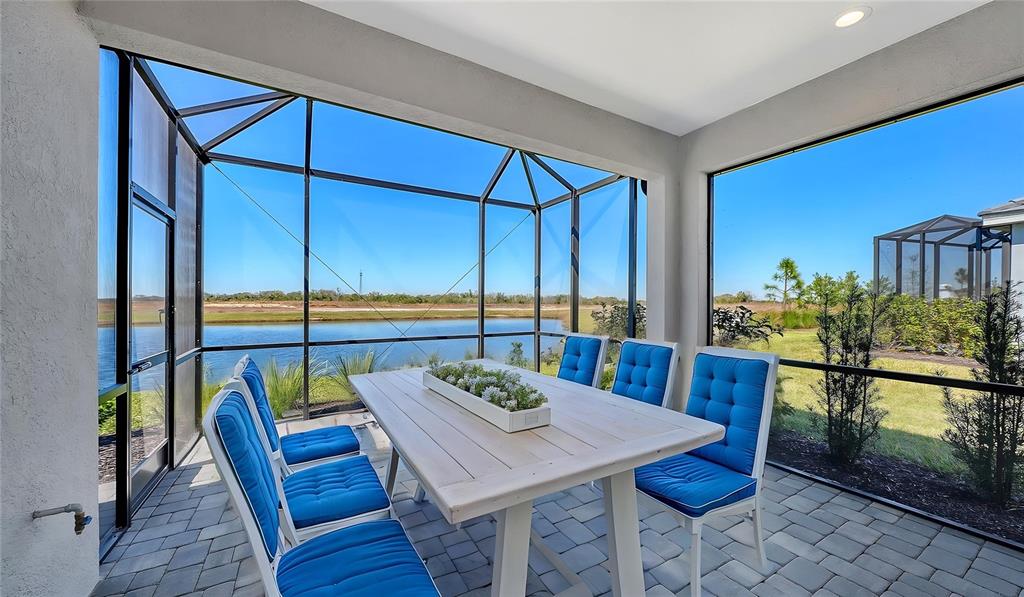 A screened-in patio features a dining table with blue chairs overlooking a pond — 2114 SYLVESTER PALM LANE, BRADENTON, FL