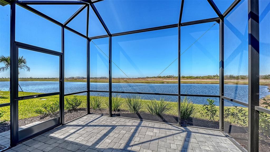 A screened-in patio with gray pavers overlooks a pond under a clear blue sky — 2114 SYLVESTER PALM LANE, BRADENTON, FL