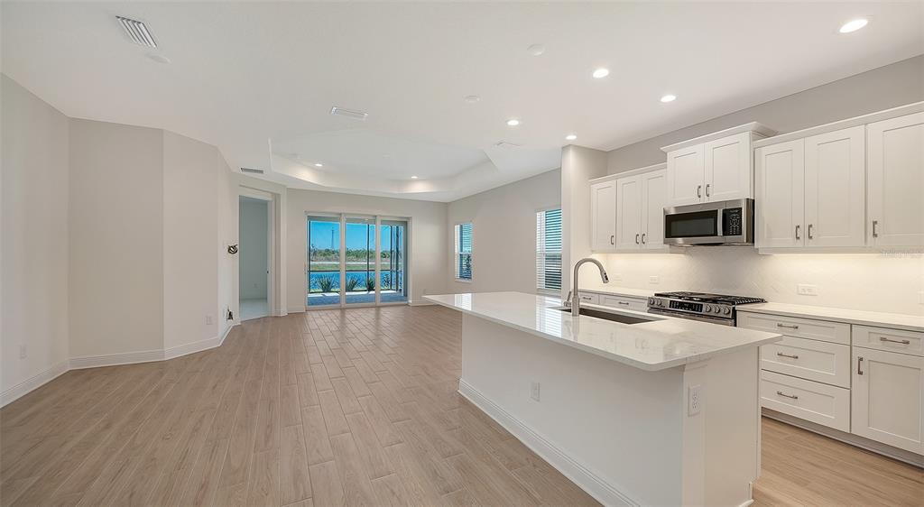 A modern kitchen with white cabinets and a quartz island opens to a living area — 2114 SYLVESTER PALM LANE, BRADENTON, FL