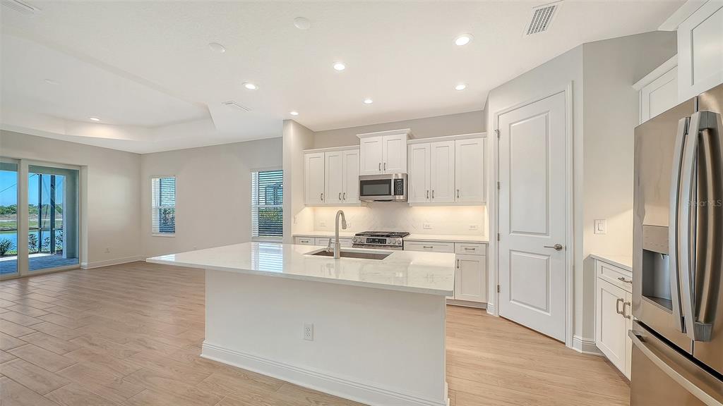 A modern kitchen features white cabinetry, a large quartz island, and light wood-look tile flooring — 2114 SYLVESTER PALM LANE, BRADENTON, FL