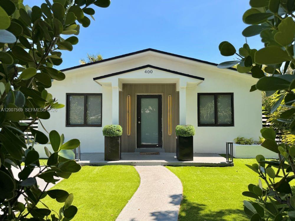 The exterior of a single-story house features a white facade, dark window frames, and landscaping — 400 NW 40th St, Miami FL 33127, MIAMI, FL